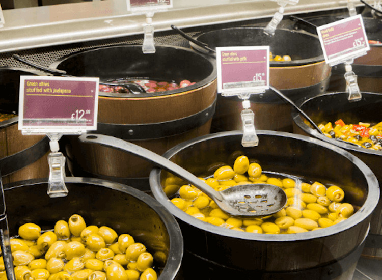 Deli counter labels with pricing on a display of olives