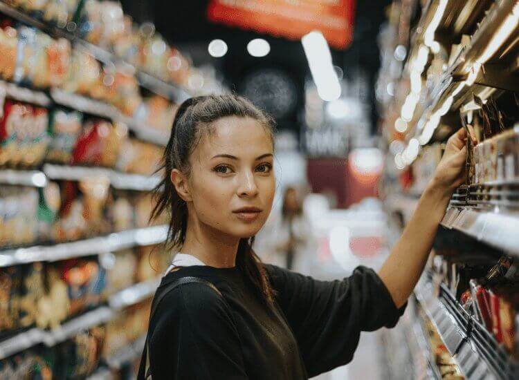 Image shows woman selecting a product from supermarket shelving